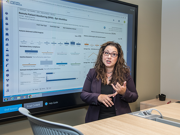 A woman stands in front of a digital presentation of data and information.